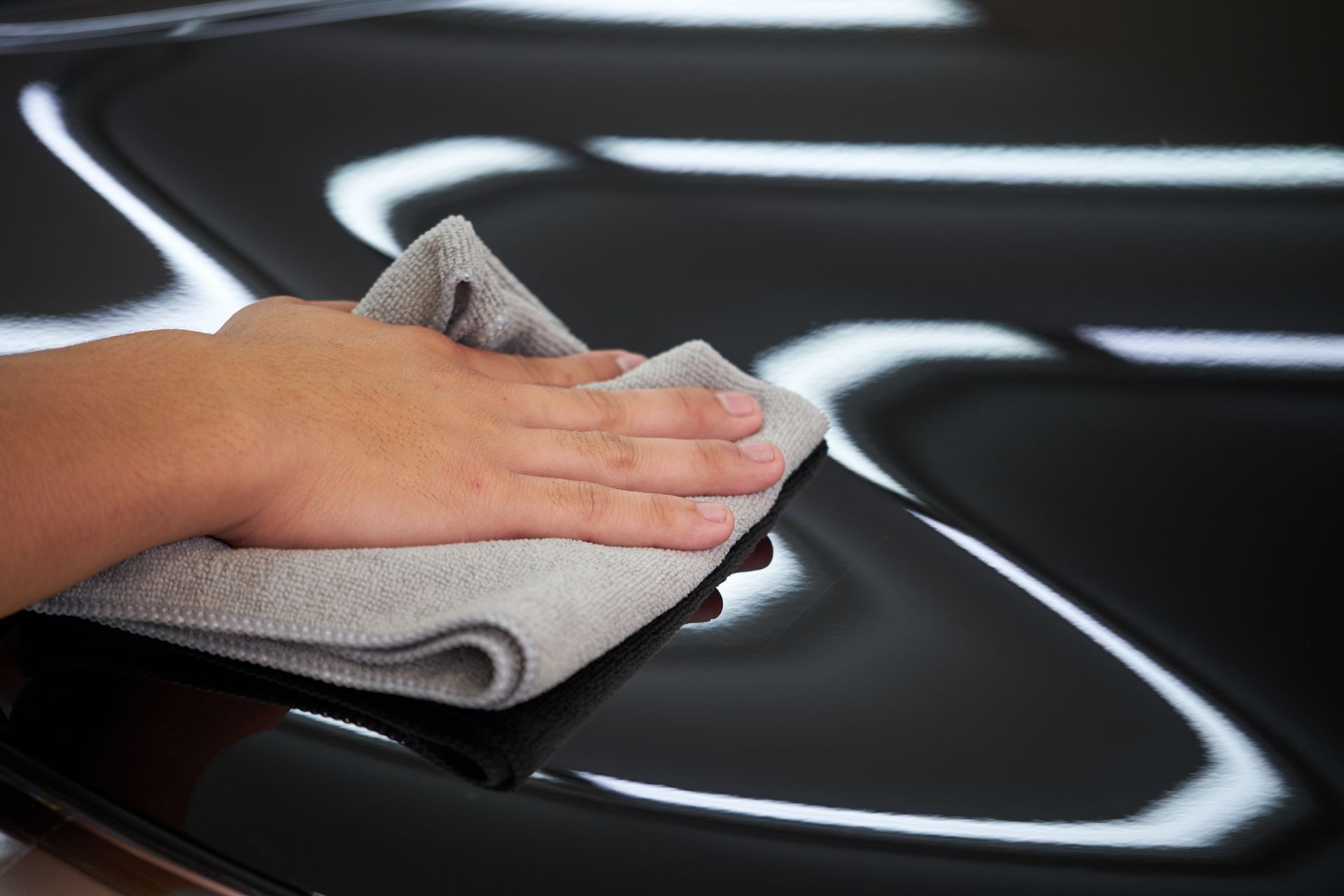 Man's hand cleaning car and drying vehicle with microfiber cloth. Hand wipe down paint surface of shiny black sedan after polishing and ceramic coating. Car detailing  and car wash concept.